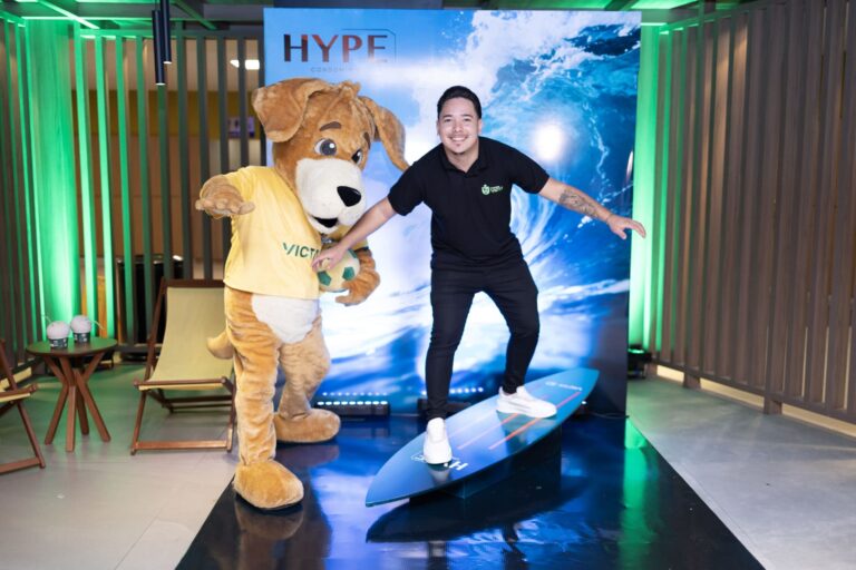 Time de vendas da victa e mascote posam sobre prancha de surfe para apresentar o novo empreendimento na praia do Futuro da marca
